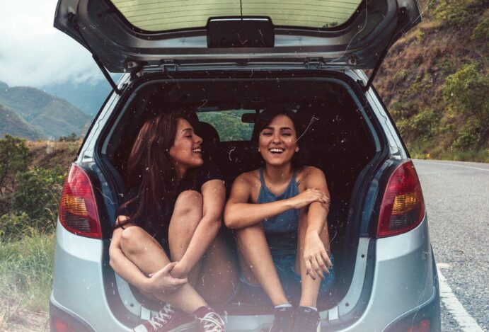 moças no porta malas aberto de um carro em viagem por estrada